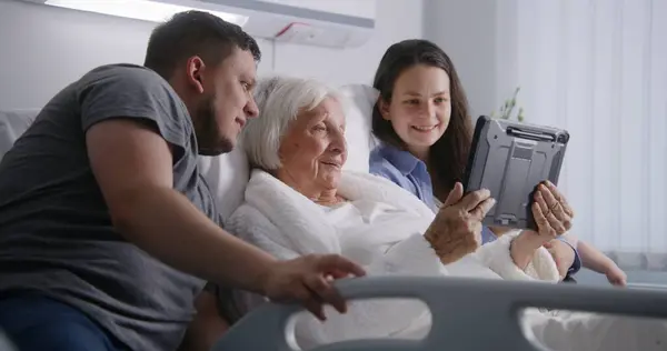 医院房间 老妇人躺在床上和亲戚呆在一起 爱的家庭使用平板电脑 支持年老的祖母在手术成功后康复 现代医疗设施或诊所 — 图库照片