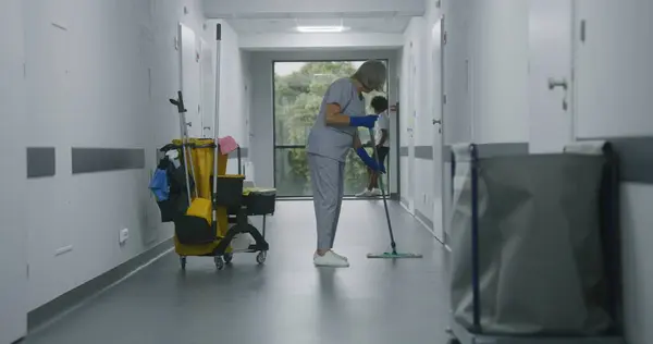 Ώριμη Καθαρίστρια Σφουγγαρίζει Όροφο Στο Ιατρικό Κέντρο Διάδρομο Πολυπολιτισμικοί Έφηβοι — Φωτογραφία Αρχείου