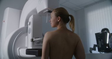 Yetişkin kadın, hastane radyoloji odasında üstsüz mammografi taraması yapıyor. Radyolog bilgisayarla mammogram makinesi kuruyor. Göğüs kanseri önleme. Modern parlak klinik.