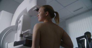Yetişkin bir kadın klinik radyoloji odasında üstsüz mammografi taraması yaptırıyor. Erkek doktor mamogram makinesini bilgisayar kullanarak ayarlar. Göğüs kanseri önleme. Modern, parlak hastane.
