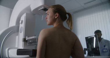 Yetişkin bir kadın klinik radyoloji odasında üstsüz mammografi taraması yaptırıyor. Erkek doktor mamogram makinesini bilgisayar kullanarak ayarlar. Göğüs kanseri önleme. Modern, parlak hastane.