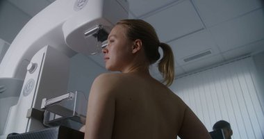 Yetişkin bir kadın klinik radyoloji odasında üstsüz mammografi taraması yaptırıyor. Erkek doktor mamogram makinesini bilgisayar kullanarak ayarlar. Göğüs kanseri önleme. Modern, parlak hastane.