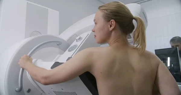 大人の女性は 臨床放射線科室でマンモグラフィのスキャン検査を受けているトップレスの立場です 男性医師はコンピュータを使ってマンモグラフィーマシンをセットアップします 乳がん予防について 現代の明るい病院 — ストック写真