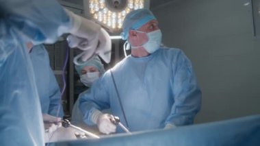 Yetişkin adam anestezi altında masada yatıyor. Profesyonel erkek cerrahlar hastalarını laparoskopi aletleriyle ameliyat ederler ve monitöre bakarlar. Genç hemşire sağlıkçılara yardım ediyor. Ameliyathanede tıbbi personel var..