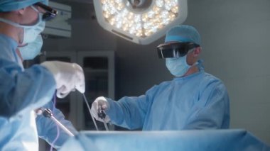 Koruyucu gözlüklü cerrahlar ameliyat sırasında laparoskopik aletler kullanıyorlar. Doktorlar ve sağlık görevlileri ciddi şekilde yaralanmış bir hastaya ameliyat yapıyorlar. Modern hastanede tıbbi personel işi..