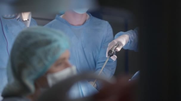 穿着外科服的专业外科医生使用现代腹腔镜器械在手术室里给病人做手术 护士或麻醉师通过监视器检查病人的病情 现代医疗设施 — 图库视频影像