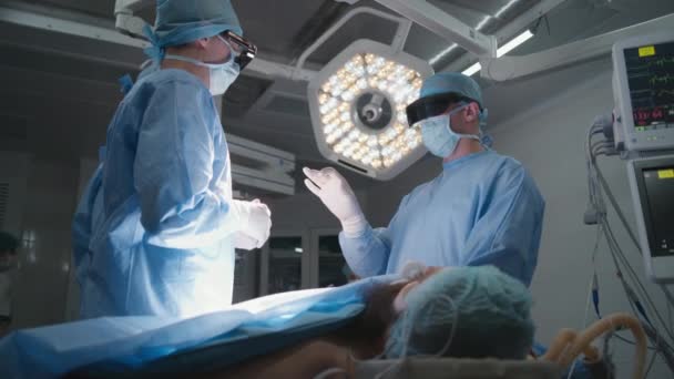 保護眼鏡の外科医チームは 患者とのテーブルの近くに立って 手術のプロセスを議論しています 看護師 救急隊員は手術の準備をする 病院で働く医療スタッフ — ストック動画
