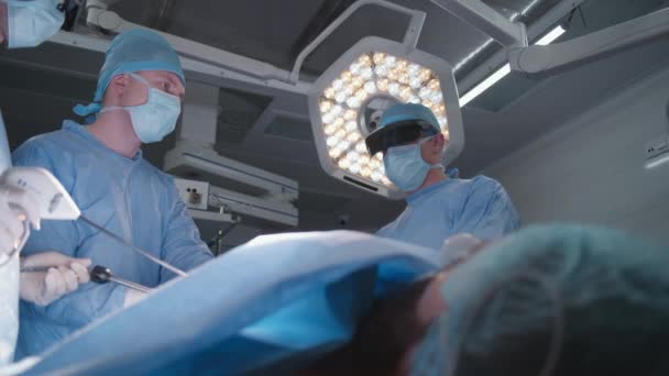 一组戴防护眼镜的外科医生在外科手术中使用腹腔镜仪器 医生和医护人员对严重受伤的病人进行外科手术 医疗人员在诊所工作 — 图库视频影像