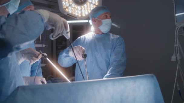 成年专业外科医生进行腹腔镜手术 并在设备齐全的手术室检查监视器 护士帮助医生 麻醉时病人躺在桌子上 有呼吸管 — 图库视频影像