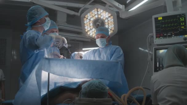 成年男子躺在桌子上 用呼吸管麻醉 男外科医生与助手一起做腹腔镜检查 年轻护士用监视器检查病人的病情 现代手术室的内科 — 图库视频影像