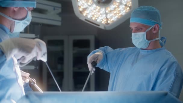 在手术过程中 一组穿着实验室外套的外科医生使用腹腔镜仪器 医生和医护人员对严重受伤的病人进行外科手术 现代医疗设施的医疗工作 — 图库视频影像
