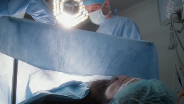 男外科医生为成年患者做手术 护士协助医生并提供医疗工具 男人躺在桌子上 在麻醉下有呼吸管 在设备齐全的手术室工作的医务人员 — 图库视频影像