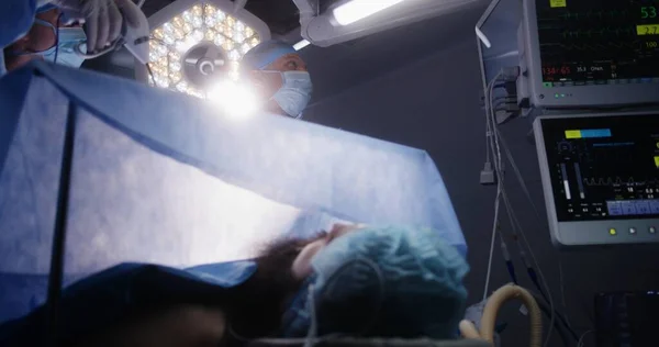 成年专业外科医生进行腹腔镜手术 并在设备齐全的手术室检查监视器 护士帮助医生 麻醉时病人躺在桌子上 有呼吸管 — 图库照片