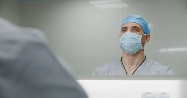 Professional surgeon in uniform cleans hands before surgery. Male medic prepares to performing surgical operation with seriously injured patient. Medical personnel work in modern hospital. Close up.