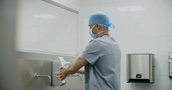 Professional surgeon in uniform washes hands before surgical operation. Paramedic or doctor prepares to performing surgery with seriously injured patient. Personnel work in modern medical facility.