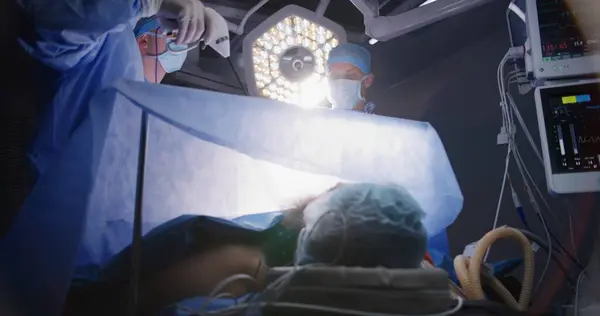大人の専門外科医は腹腔鏡検査を行い 設備の整った手術室でモニターを観察します 看護師が医師を支援する 患者は麻酔の下で呼吸チューブでテーブルの上にあります — ストック写真