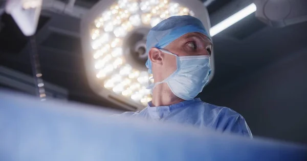 心臓移植手術を準備する実験室コートの外科医の近くに顔を合わせます 看護師 救急隊員は重傷を負った患者で手術を行う 現代クリニックの医療スタッフ — ストック写真