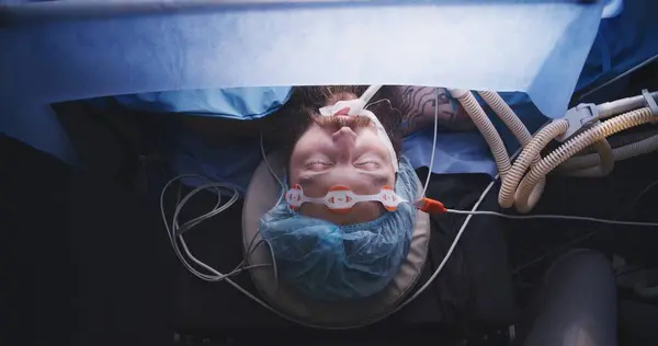 Close up top view of male patient sleeps under anesthesia on surgical table during difficult surgery in hospital. Professional surgeons operate man in modern medical facility. Heart transplantation.