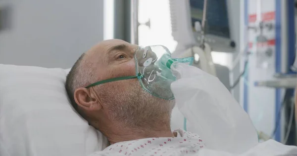 Nurse takes care of sick senior patient. Elderly man in oxygen mask lies in bed during artificial lung ventilation. Emergency room in modern hospital. Intensive care coronavirus department in clinic.