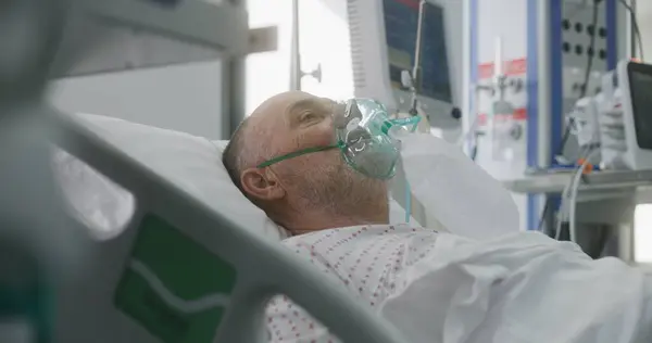 酸素マスクの高齢者は人工肺換気中にベッドに横たわっています 看護師は患者の世話をする 近代クリニックの緊急治療室 医療施設の集中治療コロナウイルス部門 — ストック写真