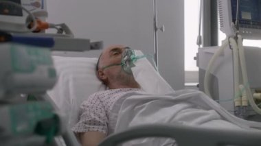 Oksijen maskeli kıdemli adam hastane koğuşunda yatıyor. Yapay akciğer solunum sırasında eski bir hasta. Klinikteki modern acil servis. Tıbbi tesiste yoğun bakım Coronavirus Bölümü.