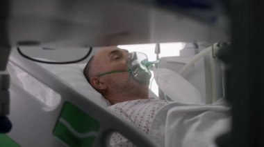 Klinikte modern ekipmanlarla acil servis. Oksijen maskeli yaşlı adam başarılı bir ameliyattan sonra yatakta yatıyor. Hemşire hastayla ilgilenir. Tıbbi tesiste yoğun bakım Coronavirus Bölümü.