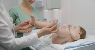 Bebek doktoruyla randevusu olan bir anne. Kadın doktor çocuğun gelişimini kontrol ediyor. Küçük çocuk, parlak hastane odasında masasını değiştiriyor. Tıp merkezinde profesyonel doktor çalışıyor..