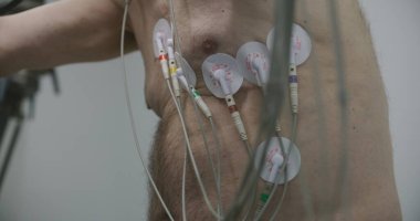 Holter sensörlü yaşlı bir adam işlevsel rehabilitasyon sırasında kardiyoloji odasında yörünge pedalları çeviriyor. Kardiyovasküler ya da kalp rahatsızlığı olan eski bir hasta. Modern tıp merkezinde elektrokardiyografi.