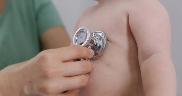 Mom holds pretty baby with pacifier on her hands. Pediatrician uses stethoscope to listen to heartbeat and lungs of handsome little kid. Doctor does checkup in modern hospital. Close up. Slow motion.