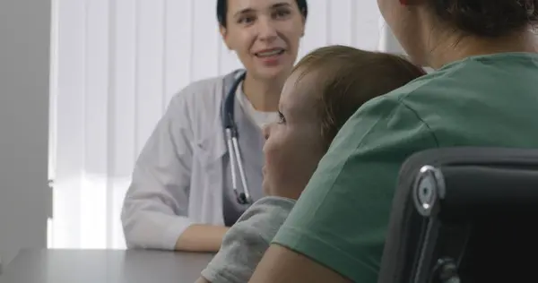 女性小児科医は 病院の予約時にかわいい小さな子供と患者に相談する 女性は医師の診察で椅子に座っている 友好的な医師は現代の医療センターで働いています クローズアップ バックビュー — ストック写真