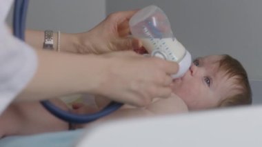 Hastanede doktor muayenesi sırasında bebeğin masadaki değişimini yakından çek. Pediyatrist küçük çocuğu bebek şişesiyle besliyor, kalp atışlarını ve tatlı çocuğun ciğerlerini dinlemek için steteskop kullanıyor..