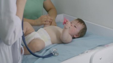 Sevimli çocuk masasını değiştiriyor, ağzından emzik çıkarıyor, el sallıyor, ağlıyor. Kadın çocuk doktoru steteskop kullanarak bebeğin kalp atışlarını dinlemeye çalışıyor. Annesi ve küçük çocuğu check-up 'ta. Kapat..