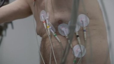 Holter sensörlü yaşlı bir adam işlevsel rehabilitasyon sırasında kardiyoloji odasında yörünge pedalları çeviriyor. Kardiyovasküler ya da kalp rahatsızlığı olan eski bir hasta. Modern tıp merkezinde elektrokardiyografi.