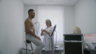 Kadın kardiyolog kalp rahatsızlığı olan hastaya holter sensör takıyor. Klinikteki kardiyoloji odasında işlevsel rehabilitasyon sırasında Afrikalı Amerikalı bir adam. Hemşire bilgisayardaki elektrokardiyogramı izliyor..