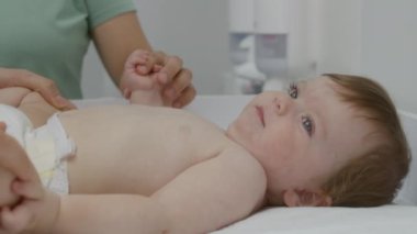Bebeğin üzerini değiştirip annesinin elini tutmasına yakın durun. Hastane koğuşundaki küçük çocuğun kalça eklemlerinin gelişimini kadın doktor kontrol ediyor. Çocuk doktoruyla randevusu olan çocuklu bir kadın..