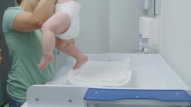 Kadın küçük çocuğu kucağına alıyor ve onu masa değişimine sokuyor. Kadın doktor, bebeği tartıyor. Parlak hastane odasında çocuklu bir anne çocuk doktoruyla randevuda. Klinikte çalışan tıbbi personel.