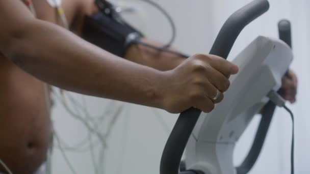 テノメーターとホルターセンサーを持つアフリカ系アメリカ人男性は 機能リハビリテーション中に心臓室の軌道レックをペダルします 心臓病の患者さん 現代医療センターにおける電気泳動 — ストック動画
