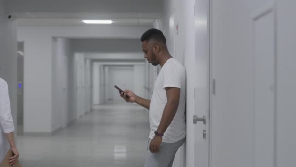 아프리카계 미국인 남자는 복도에 메시지를 전화로 진료소에서 환자를 의료진은 배경으로 — 비디오