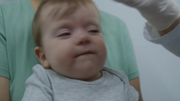 赤ちゃんは母親の腕に座って泣いている 女性医師は明るい病院の病棟で小さな男の子の歯をチェックしようとします 小児科医との面会で子供と一緒にいる女性 クリニックで働く医師 クローズアップ — ストック動画