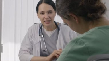 Steteskopla boyun muayenesi yapan kadın bir pediyatrist. Hastane odasında randevusu var. Kadın doktor kontrolünde sandalyeye oturmuş ve kucağında küçük bir bebek tutuyor. Dost canlısı doktor klinikte çalışıyor..