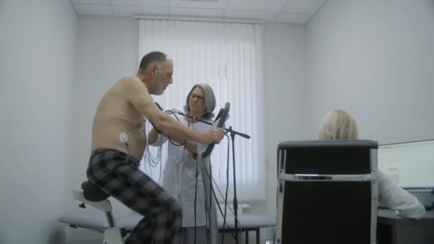 자전거와 의사는 심장학실에서 검진을 합니다 간호사는 컴퓨터에서 심장계를 모니터링합니다 클리닉에서의 — 비디오