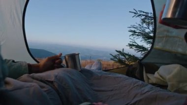 Romantik gezgin çift dağ tepesinde çadırda yatar ve çay içerler. İki turist macera tatili sırasında battaniye altında dinleniyor. Sırt çantalı aile soğuk rüzgârlı havada ısınır ve manzaraya hayran kalır..