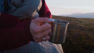 Kadın turistin elinde fincanla elinde çay resmi. Sırt çantası yürüyüş sırasında dinlenmek için durdu. Kadın dağ tepelerindeki günbatımına ve güzel manzaralara hayran. Gezgin hafta sonu tatilinde..