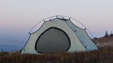 Güzel dağ tepesine gezgin çadırı kuruldu. Turistler yürüyüş sırasında ısınmak ve dinlenmek için durdular. Çadır ve yeşillik güçlü rüzgarla sallanıyor. Rüzgarlı soğuk hava. Harika manzaralı bir kamp alanı..