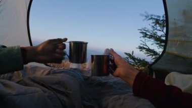 Romantik turist çiftler dağ tepesinde çadırda uzanır, bardaklarını tokuşturur ve çay içerler. İki gezgin macera tatili sırasında battaniye altında dinleniyor. Yürüyüş ailesi soğuk havada ısınır ve manzaraya hayran kalır..