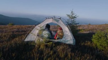 Çok ırklı turist çiftler dağ tepesinin tepesindeki çadırda oturur: Konuşur ve çay içerler. İki gezgin macera tatili sırasında dinlenmek için durdu. Romantik yürüyüşçü ailesi manzaraya hayran. Arka plan.