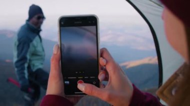 Kadın, güzel bir dağ manzarasında telefon kullanarak yürüyüşçünün resmini çekiyor. Elinde balta olan Afrikalı Amerikalı turist tepede poz veriyor. Gezginler macera tatili sırasında dinlenmek için durdular. Kapat..