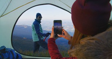 Genç bir kadın telefon kullanarak güzel bir dağ manzarasında turistin fotoğrafını çekiyor. Elinde balta olan Afrikalı Amerikalı yürüyüşçü tepede poz veriyor. Sırt çantalı arkadaşlar macera tatili sırasında dinlenmek için durdular..