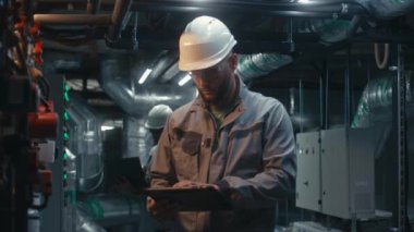 Çeşitli fabrika uzmanları dizüstü bilgisayar ve tablet bilgisayar kullanarak modern fabrika üzerinde çalışıyorlar. Güvenlik üniforması giyen endüstriyel işçiler boru hattını denetliyor. Ağır sanayi konsepti.