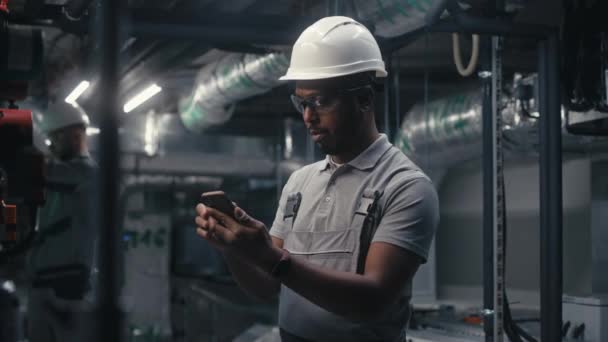 Ingeniero Afroamericano Utiliza Teléfono Móvil Para Inspeccionar Sistema Tuberías Planta — Vídeos de Stock